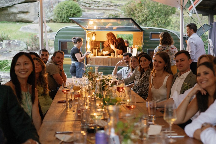 Outdoor wedding reception at Laurel Falls with guests seated at a long table near a vintage bar trailer
