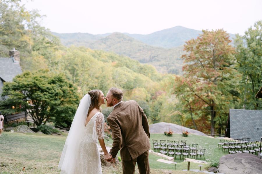 Bride and groom leaning in for a kiss during their wedding portraits with mountain views and their ceremony chairs in the background.