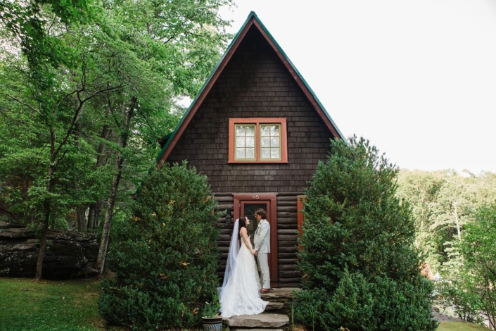 Bride and groom holding hands in front of a rustic A-frame cabin surrounded by lush forest at Laurel Falls wedding venue.