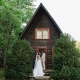 Bride and groom holding hands in front of a rustic A-frame cabin surrounded by lush forest at Laurel Falls wedding venue.