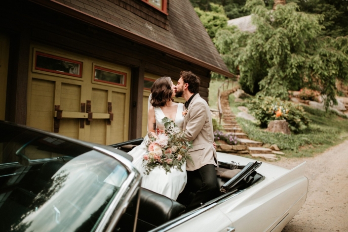 Bride and groom kissing in a vintage convertible outside The Carriage House at Laurel Falls.