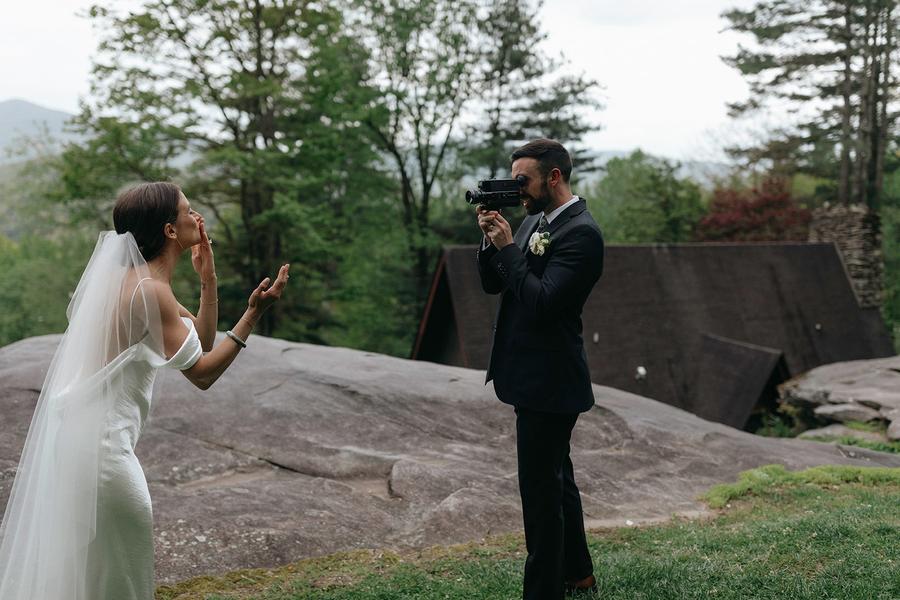 Bride and groom sharing a playful moment with a vintage camera on a rock at Laurel Falls