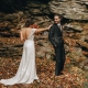 Bride taps groom on the shoulder during a first look on a rocky outcrop surrounded by autumn leaves.