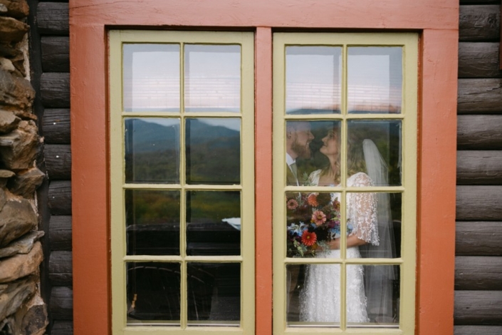 Bride and groom seen through cabin window at Laurel Falls with mountain reflection