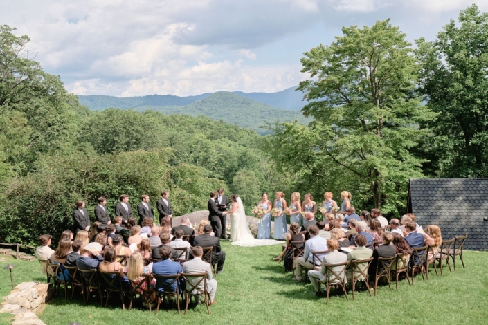 Outdoor mountain wedding ceremony at scenic wedding venue with lawn seating, bride and groom exchanging vows overlooking Blue Ridge Mountain views.